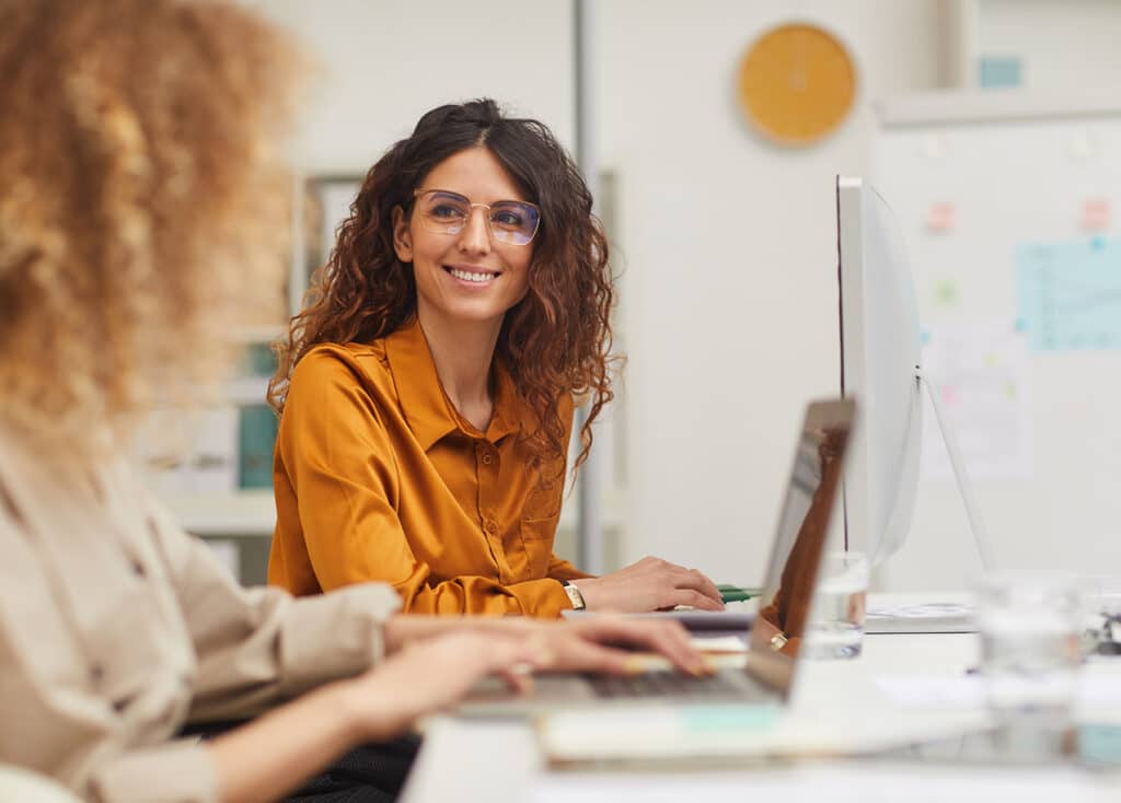Two female colleagues interacting while working in office